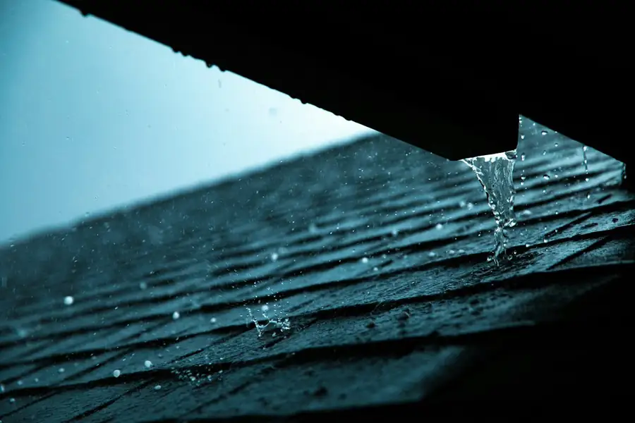 Rain running off a shingled roof edge into a gutter